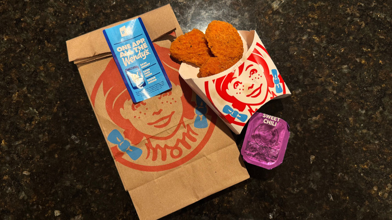 Sleeve of Wendy's Spicy Chicken Nuggets and sweet chili sauce cup resting on to-go baggie