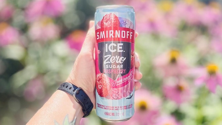 Hand holding can of Smirnoff Ice Zero Sugar Raspberry in front of blurred flowers
