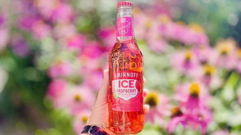 Hand holding can of Smirnoff Ice Raspberry in front of blurred flowers
