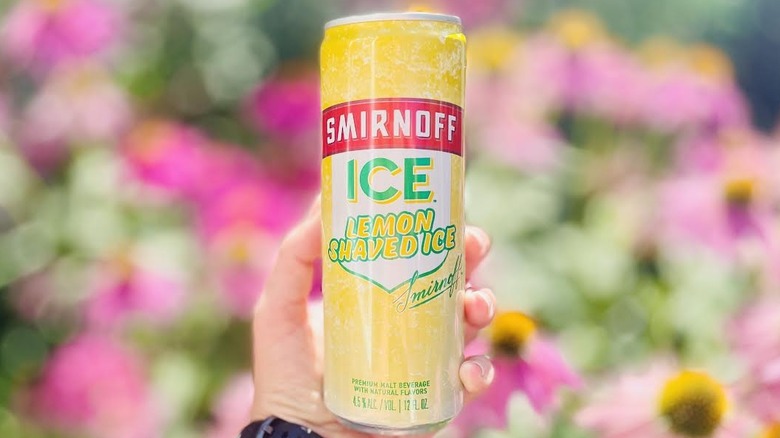 Hand holding can of Smirnoff Ice Lemon Shaved Ice in front of blurred flowers