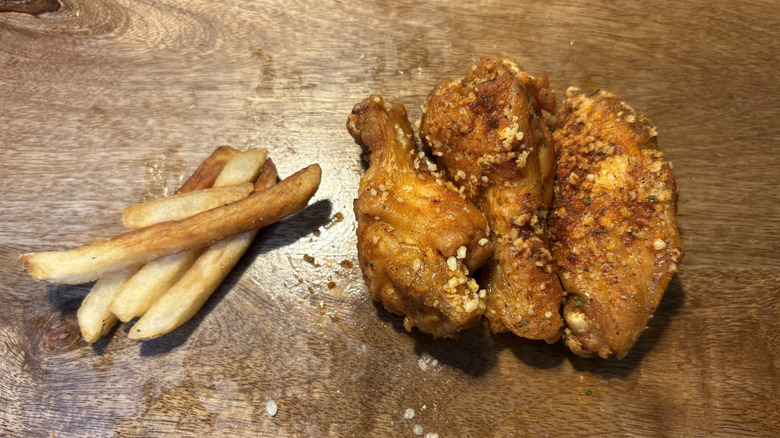 Three Mexican Street Spice bone-in wings and fries on brown wooden table