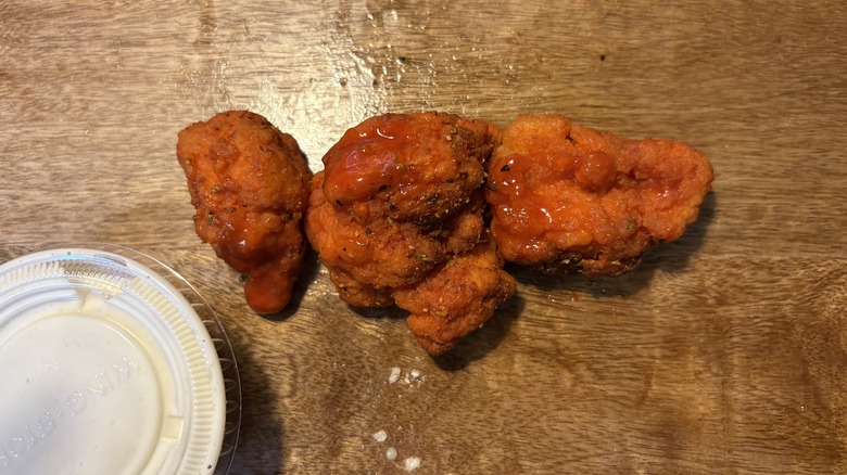 Three Cajun boneless wings and sauce cup on brown wooden table