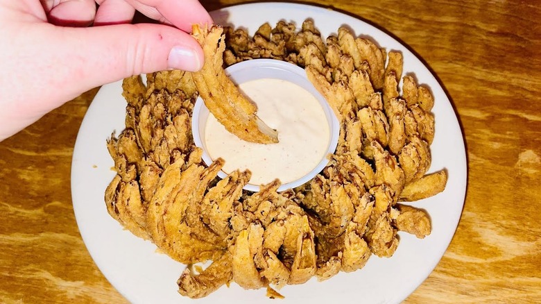 A hand is dipping a piece of Texas Roadhouse Cactus Blossom in sauce.