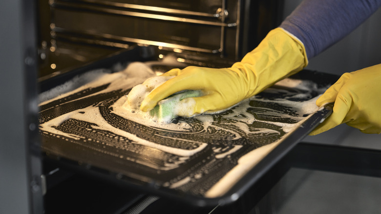 A person wearing gloves wiping the inside of the oven with a soap and sponge