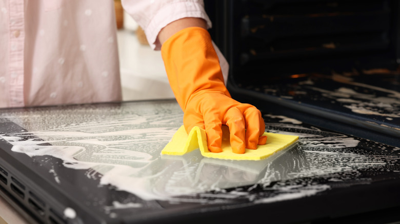 A woman wears a rubber glove while cleaning an oven door.