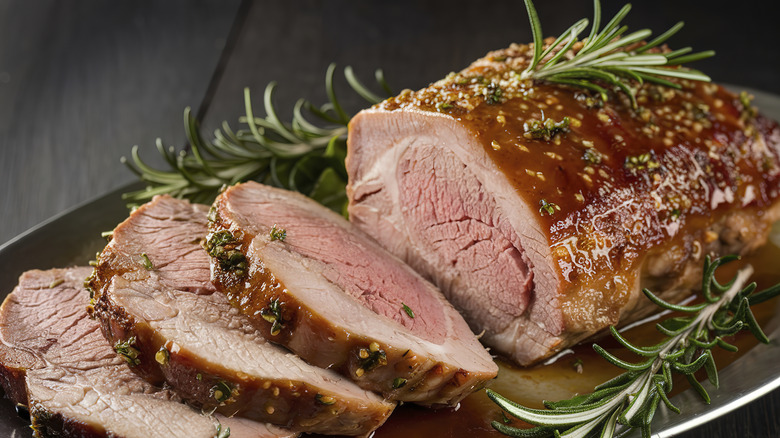 cooked pork sliced on a plate with rosemary garnish