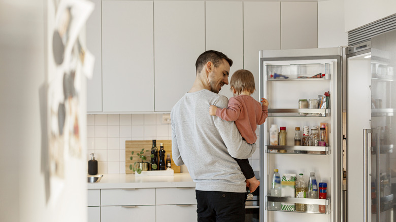 man holding baby looking into fridge