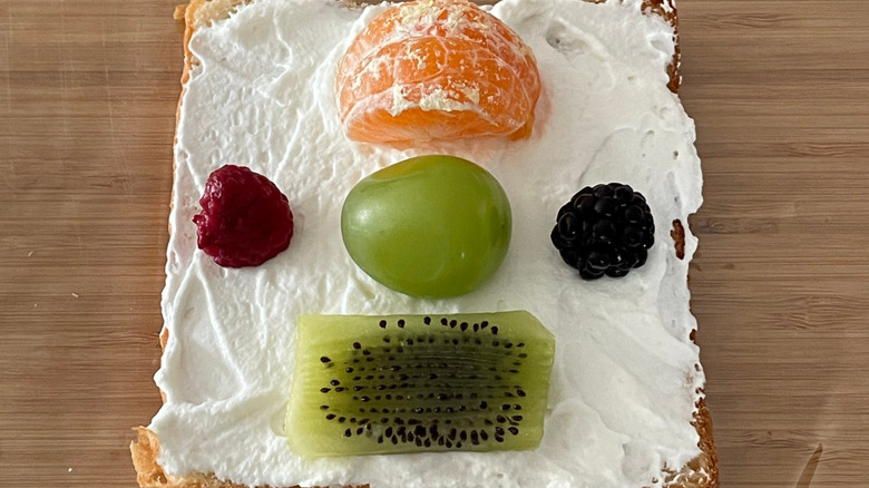 A fruit sandwich before the top bread showing a raspberry, grape, blackberry, orange, and kiwi