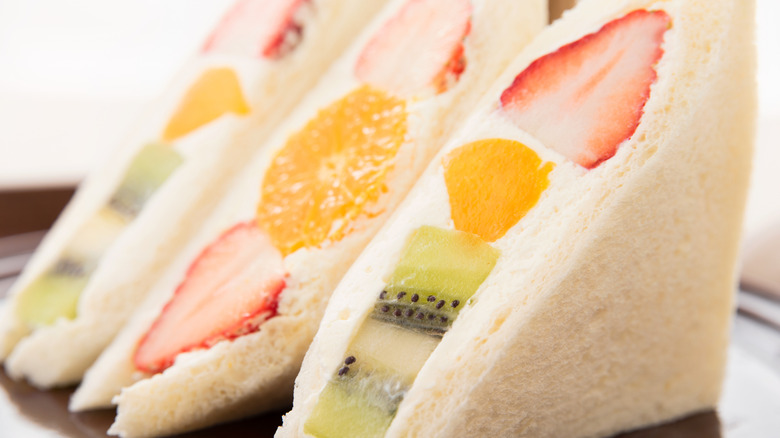 A plate with sliced fruit sandwiches with strawberries, oranges, and kiwi
