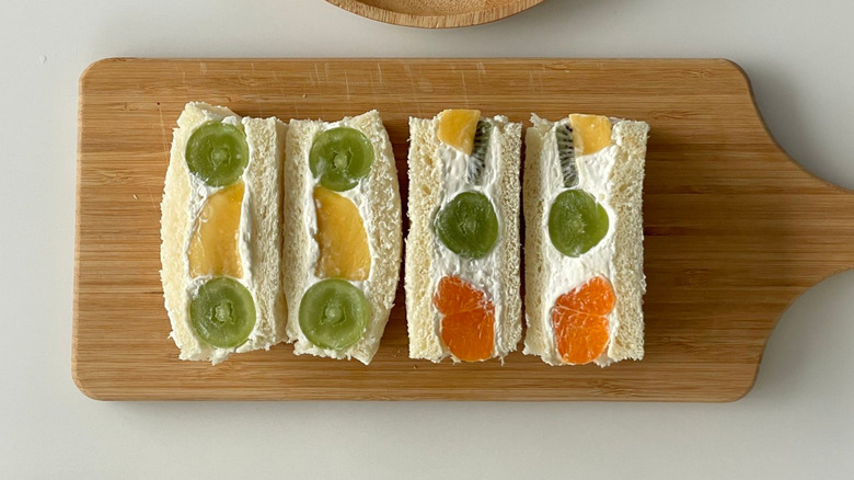Sliced fruit sandwiches with kiwi and orange on a wooden cutting board