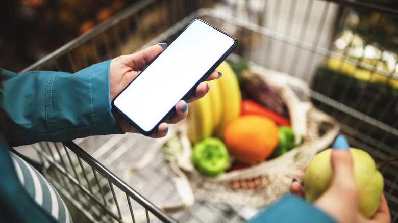 person holding phone and checking out produce