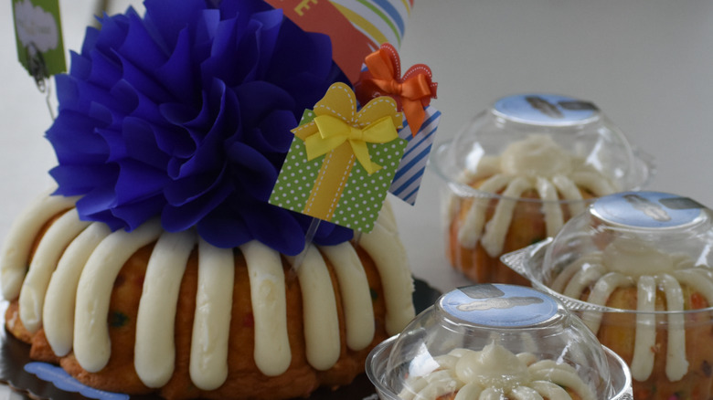 A bundt cake decorated for a birthday with a smaller bundt cake in a to-go container in front