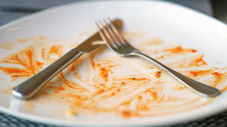 A fork and knife rest on a white plate with a bit of tomato sauce left.