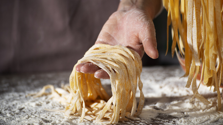 A hand holds fresh pasta noodles in flour.