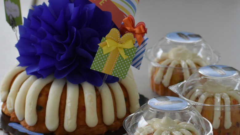 A bundt cake decorated for a birthday with a smaller bundt cake in a to-go container in front