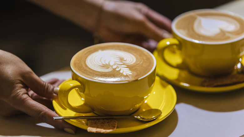 A barista's hand serving two lattes on a counter.