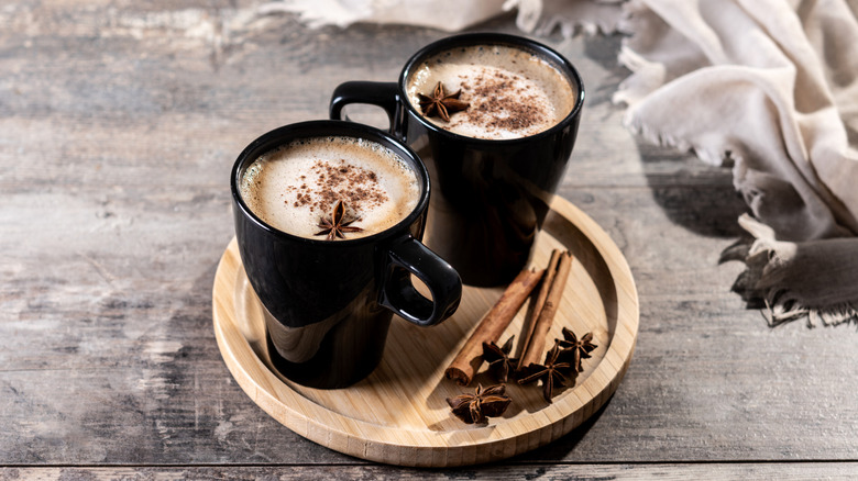 Two chai lattes on a wooden tray with spices.