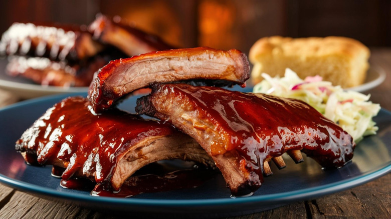 Saucy barbecue ribs are stacked on a blue plate.