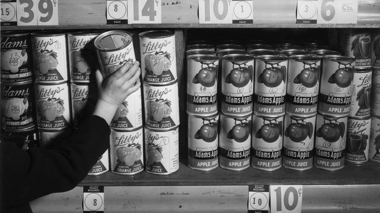 Black and white photo of a person taking a can of Libby's orange juice off a store shelf