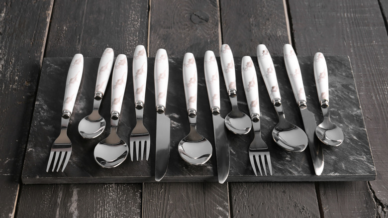 Stainless steel cutlery lined up on a wooden board.