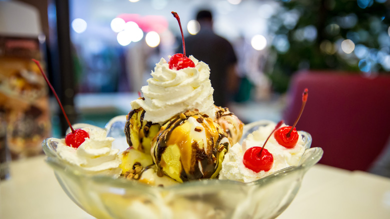 Large ice cream sundae with whipped cream and cherries in a glass bowl sitting on a table