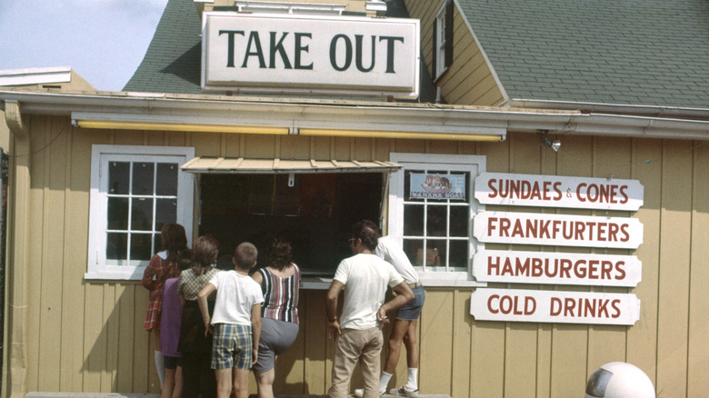 The outside of a building with a take out sign above the window where people are ordering.