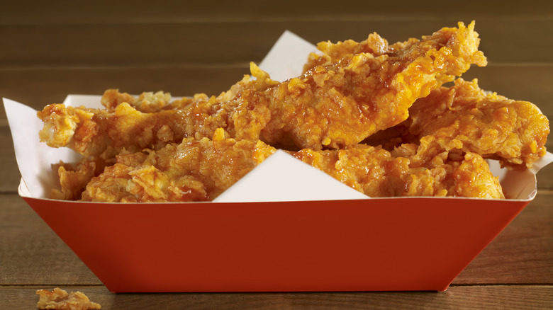 A red basket of chicken fingers with sauce on them.