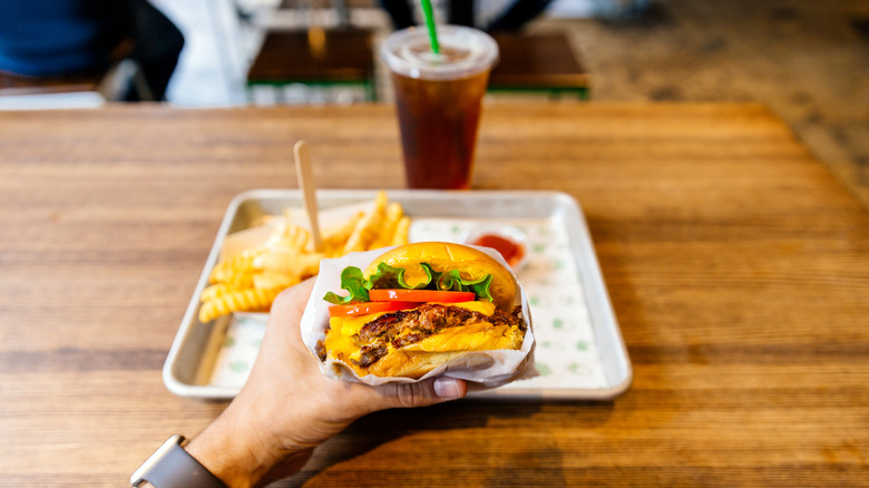Hand holding a fast food hamburger in front of a table