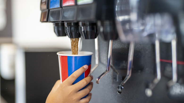 Person filling a soda cup from a fountain