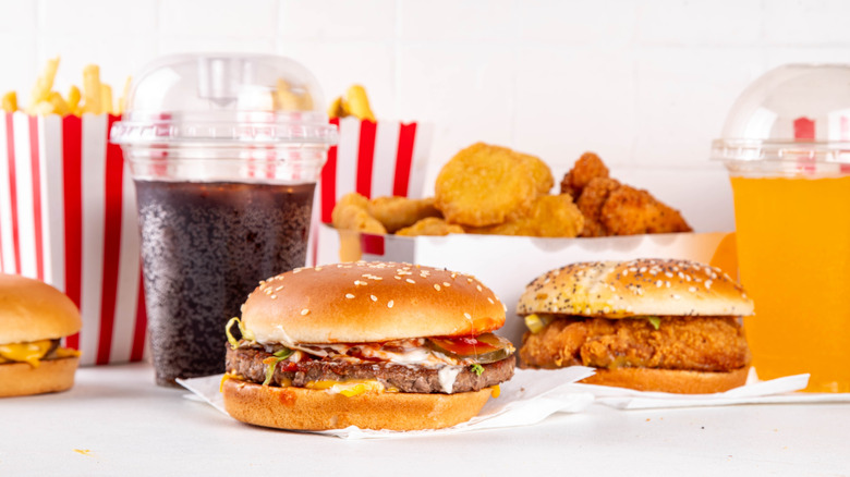 Fast food burgers, chicken nuggets, fries in striped containers, and sodas against a white background