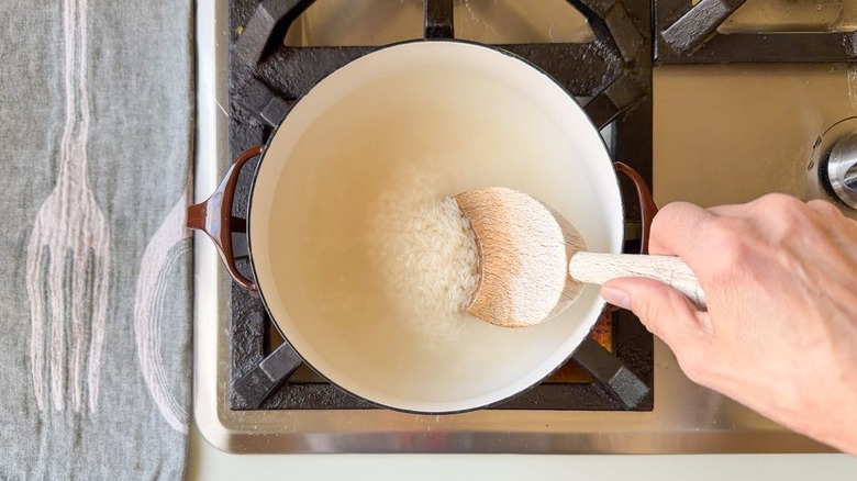 Stirring rice into water with wooden spoon in brown pot on stovetop