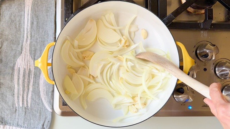 Sliced onion and smashed garlic cloves cooking in yellow pot on stovetop