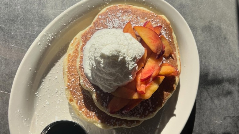 Stack of buttermilk pancakes topped with sliced peaches and whipped cream