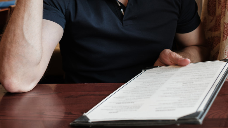 A person's hands are seen holding a restaurant menu at a table.