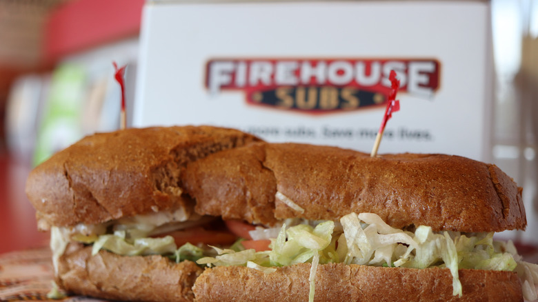 A large sub on wheat bread in front of a takeout bag from Firehouse Subs