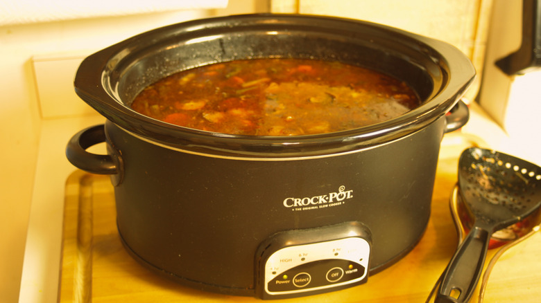 Oval Crock-Pot slow cooker with a finished stew inside and a spatula on the counter for stirring.