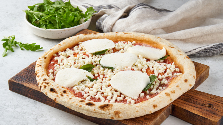 Raw frozen pizza on wood block with bowl of basil