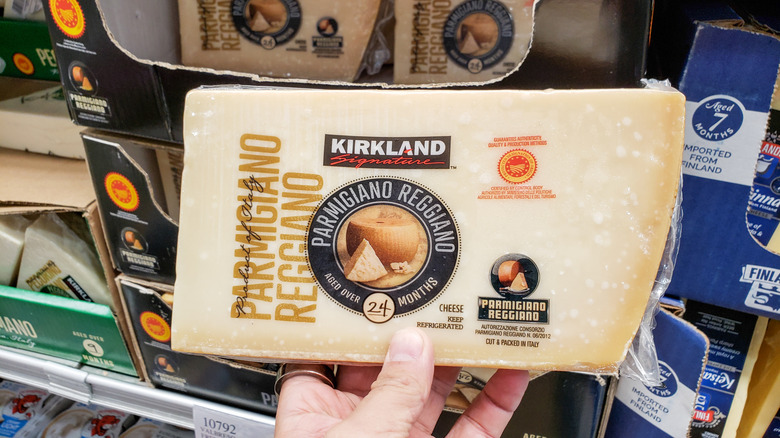 A person holding a wedge of Kirkland Signature Parmigiano Reggiano at a Costco warehouse