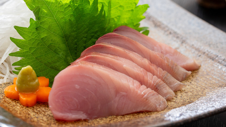 sliced bonito sashimi with a garnish of shiso leaf, carrot, wasabi, and grated radish