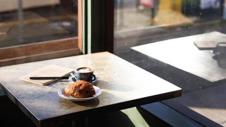 A pastry and a cappuccino sitting on a table near a window in Herkimer Coffee's Phinney Ridge location in Seattle.