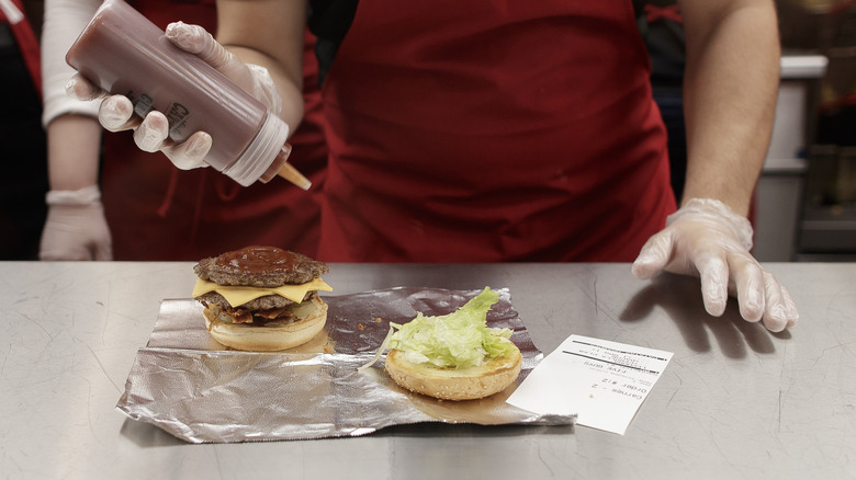 Five guys employee putting sauce on a burger