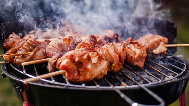 Meats on wooden skewers cooking over a smoky grill