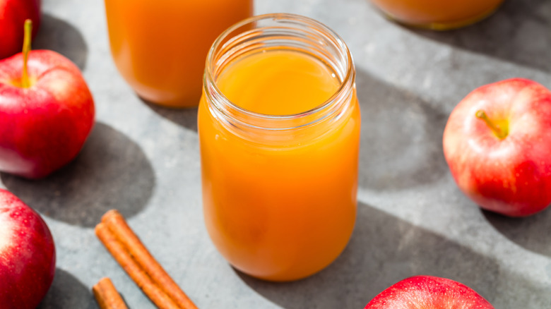 Jar of apple cider surrounded by apples and cinnamon sticks