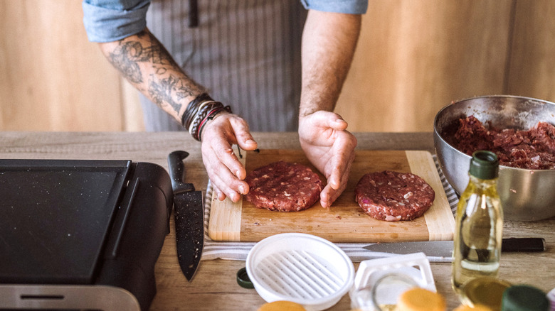 Young man Making Burgers Out Of Beef, Forming Shapes Carefully at Domestic Kitchen