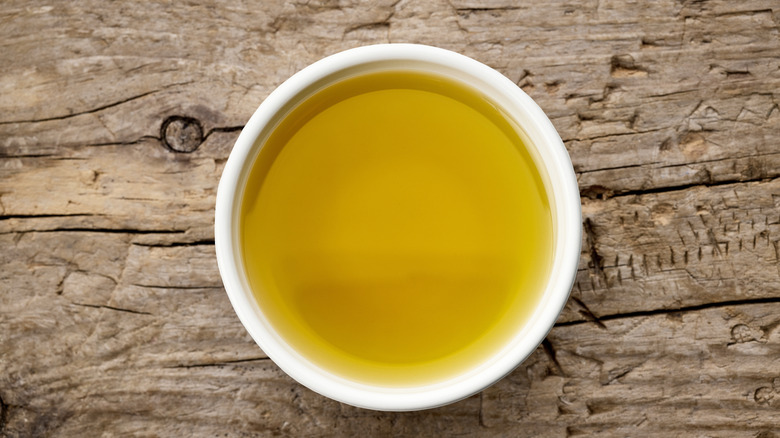 bowl of olive oil on rustic wooden kitchen table board, top view