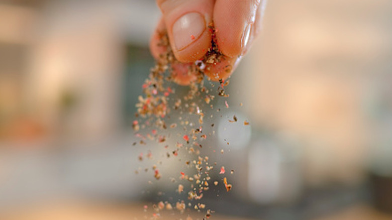 A person adding a pinch of seasoning.