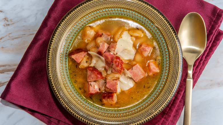 A bowl of bean soup topped with large chunks of ham