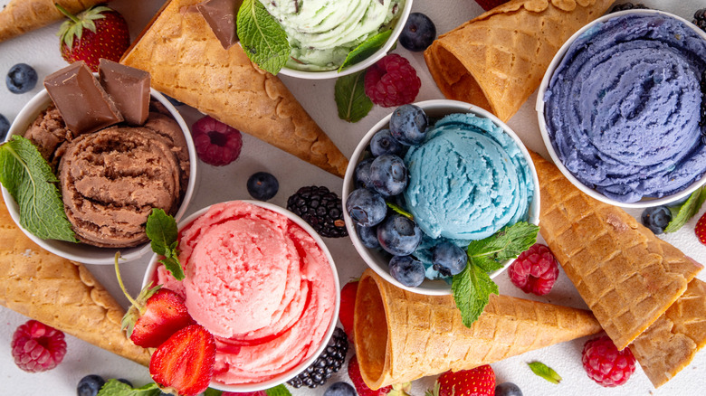 scoops of colorful ice creams in cups next to cones