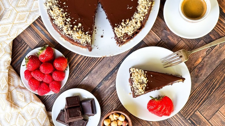 Flourless Italian gianduja chocolate cake on serving platter with slice on plate, chocolate, and berries