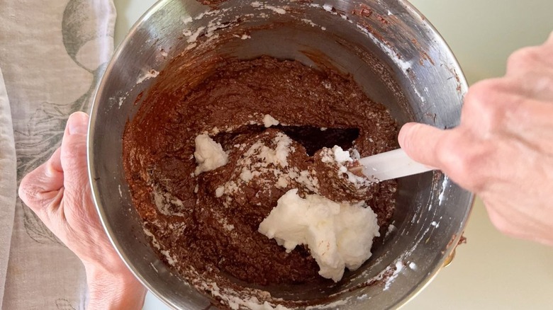 Folding whipped egg whites into chocolate hazelnut cake batter with spatula in mixer bowl